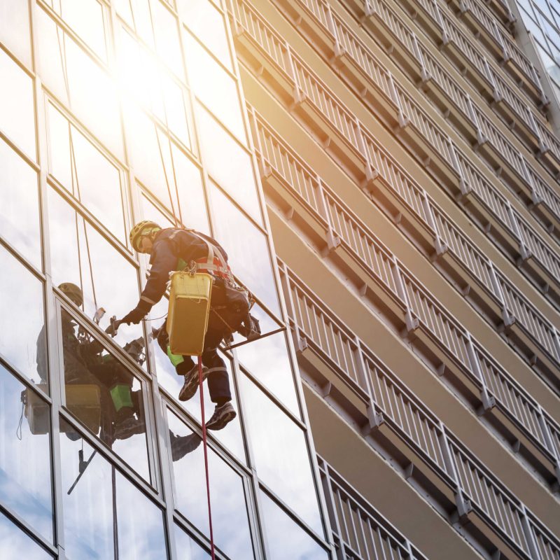 Group Industrial mountaineering workers in uniform hangs over residential facade building while washing exterior glazing. Rope access laborers hangs on wall of house. Concept of industry urban works